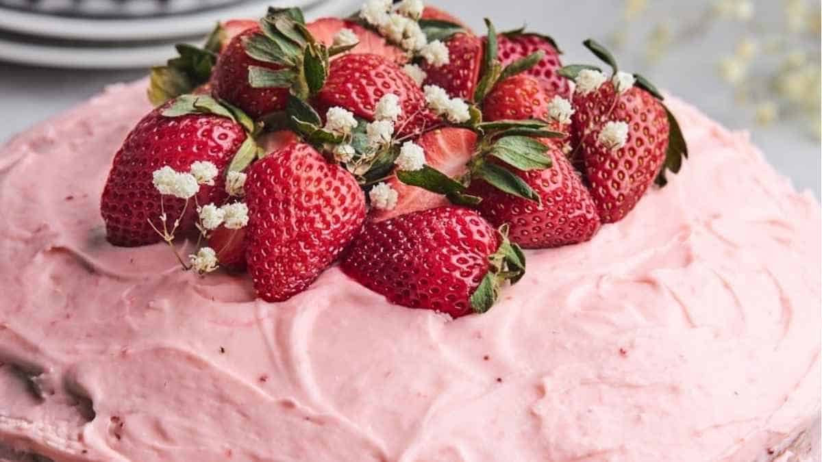 A pink frosted cake with strawberries on top.
