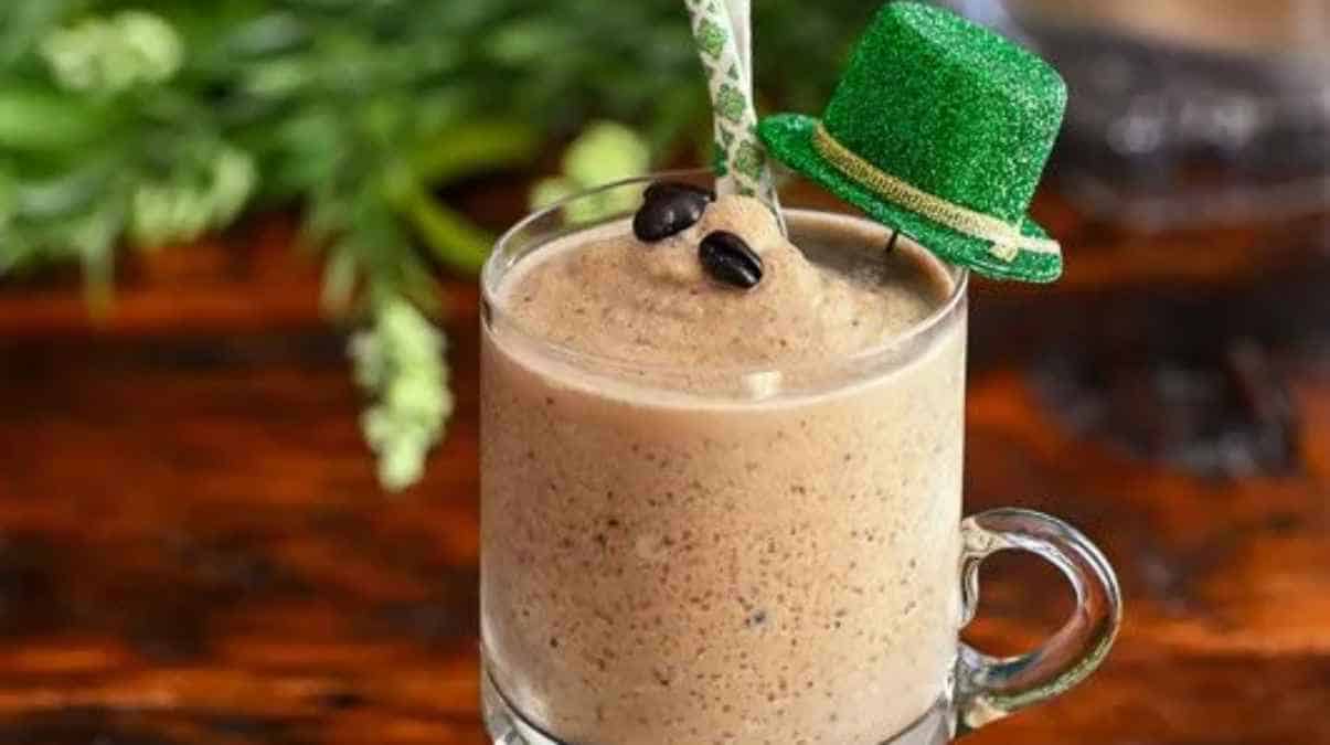 A festive coffee drink garnished with coffee beans and a miniature green top hat, likely celebrating st. patrick's day.