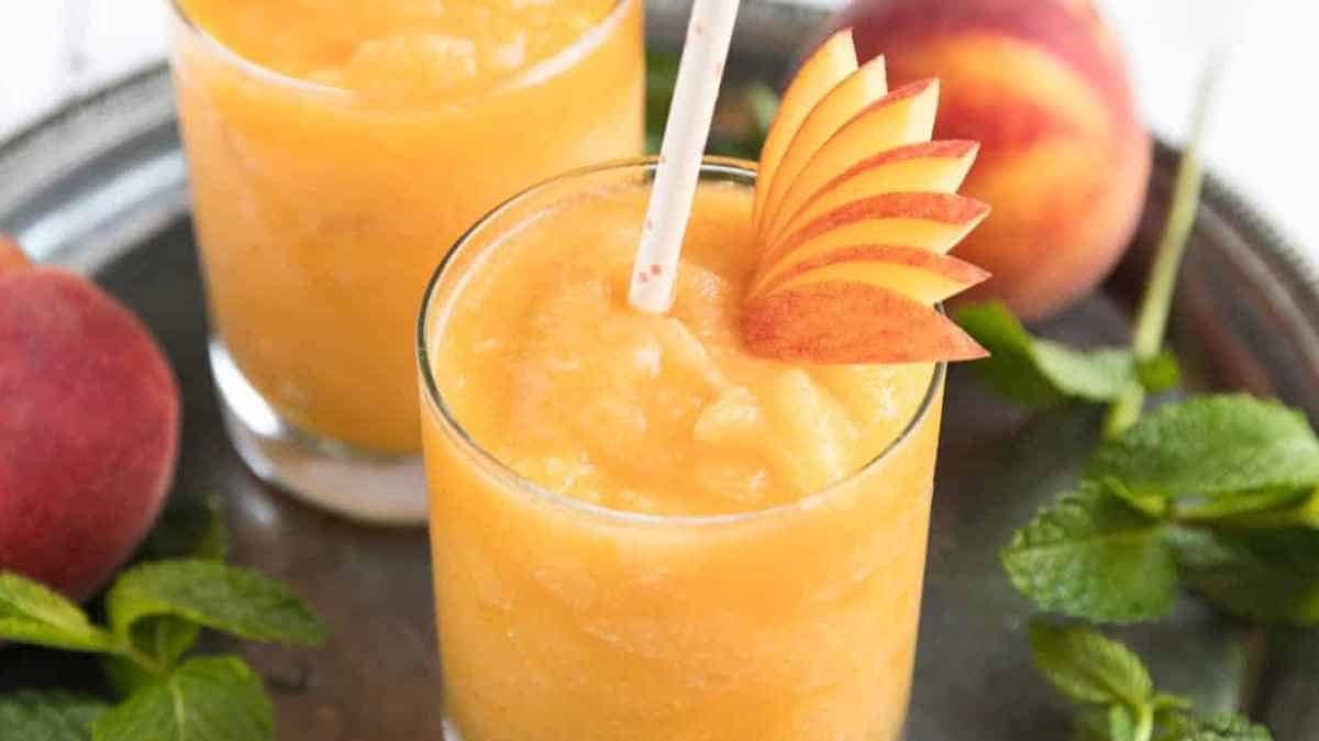 Two glasses of peach smoothie garnished with peach slices and mint leaves.