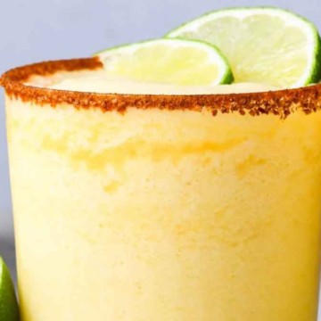 Two glasses of pineapple smoothie garnished with lime slices and a spice-coated rim, with a pineapple in the background.