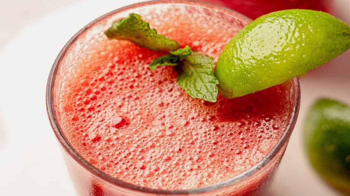 A close-up of a fizzy red drink garnished with a lime wedge and mint leaf.