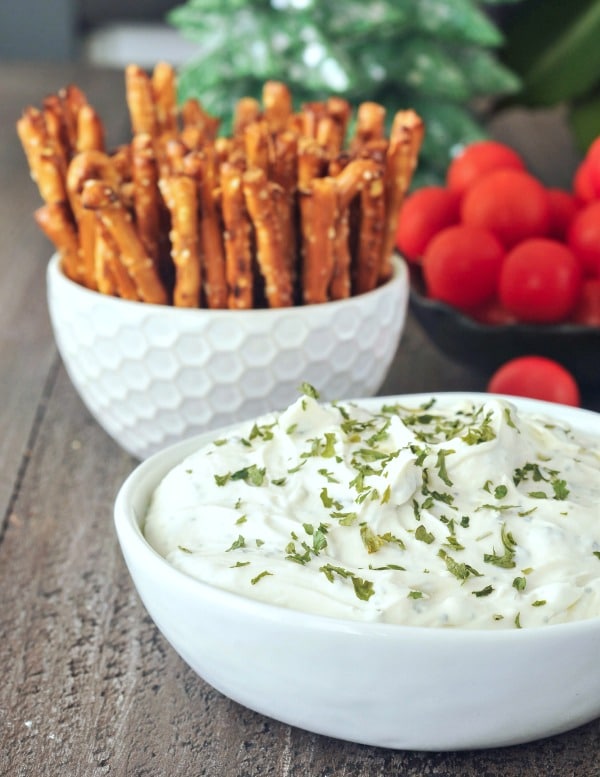 vegan Herb Cheese spread in a white ceramic serving bowl, pretzels and vegetables for dipping. 