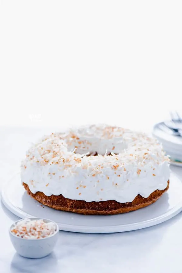 Gluten Free Coconut Pound Cake with Coconut Frosting and Toasted Coconut on a flat white cake plate.
