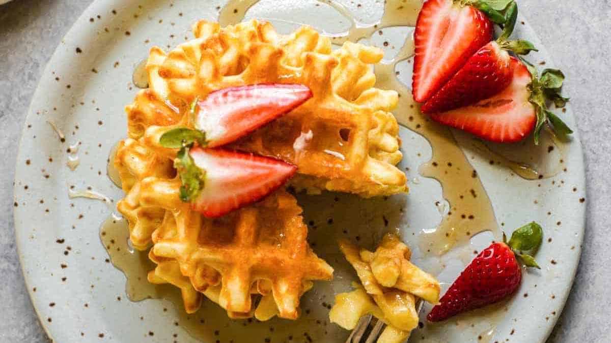 Waffles with syrup and fresh strawberry slices on a speckled plate.