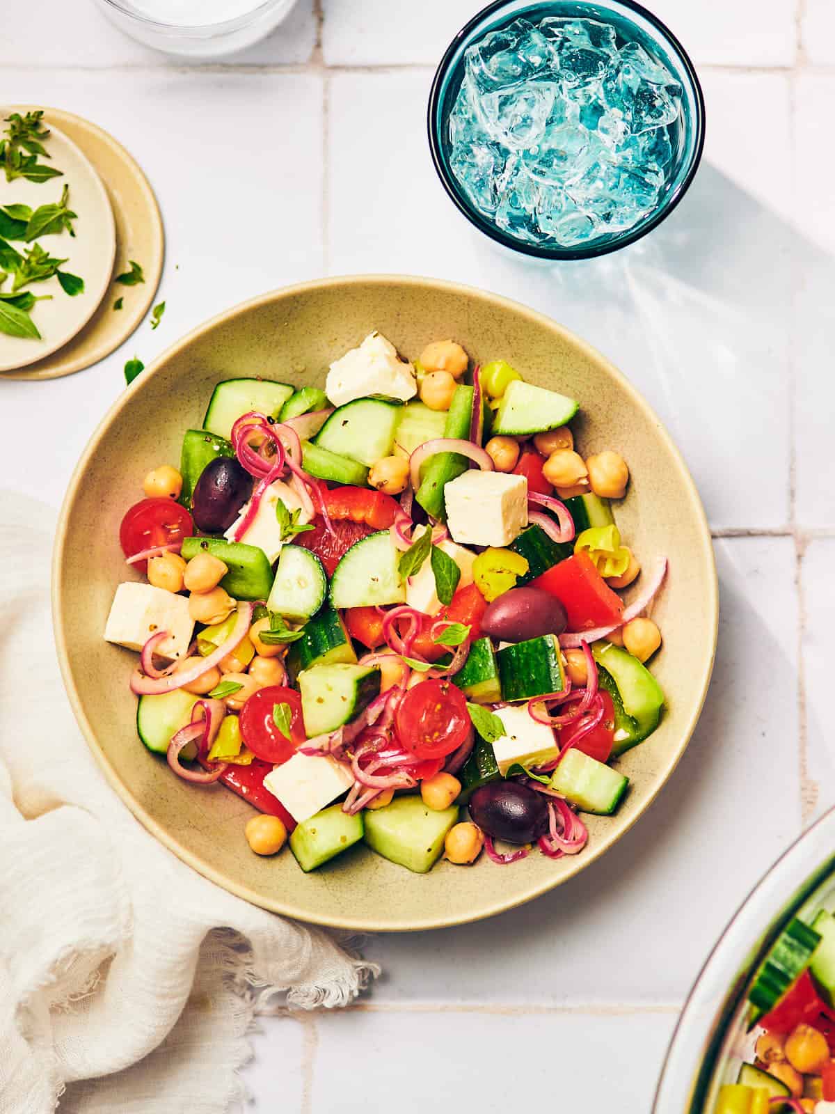 Greek cucumber salad with feta in a bowl on a table with fresh oregano. 
