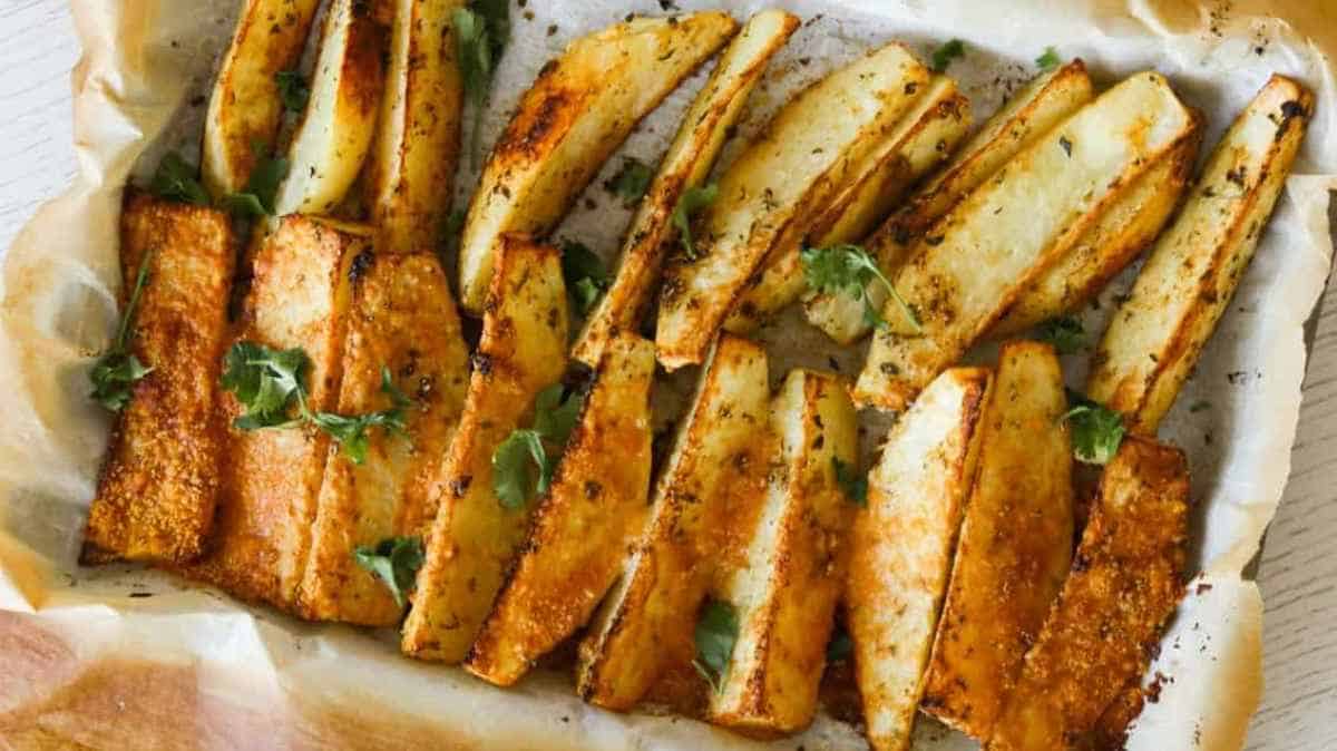 Seasoned potato wedges garnished with parsley on parchment paper.