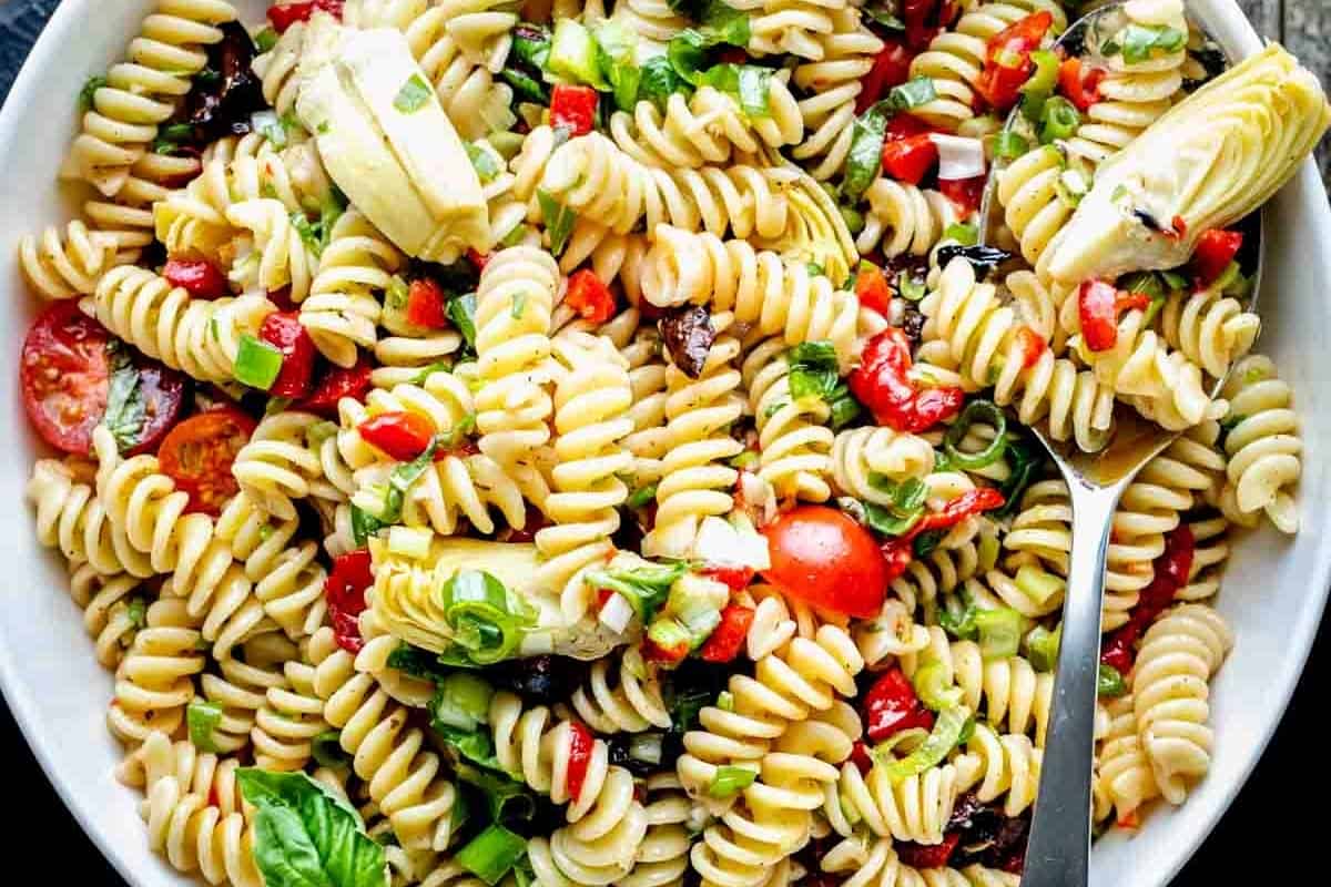 A bowl of pasta salad with tomatoes and olives.