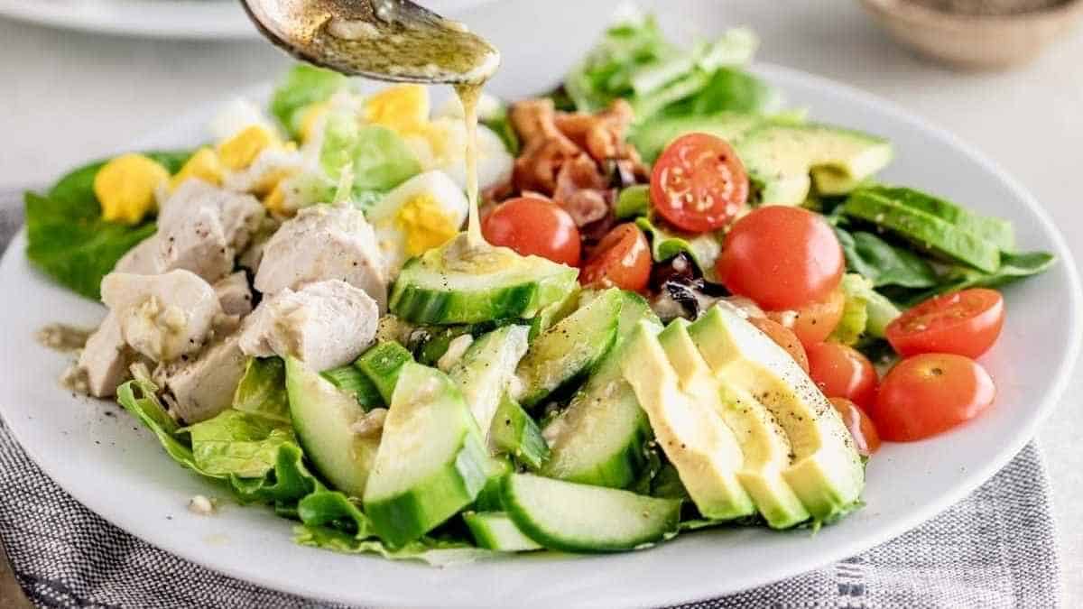 A salad with chicken, avocado and tomatoes being drizzled with dressing.