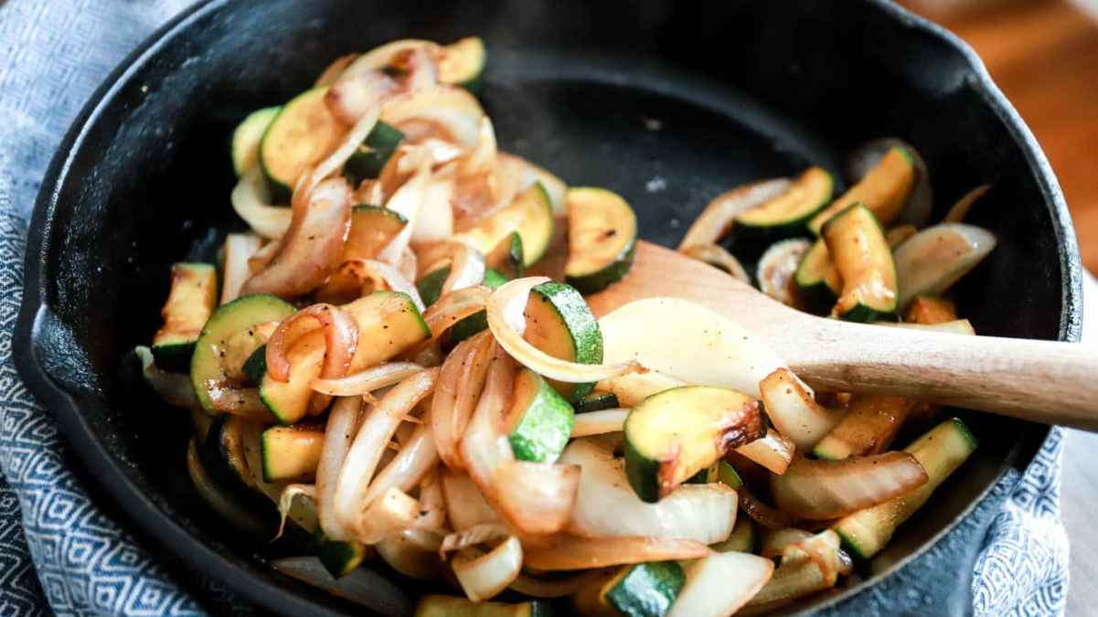 Sautéed zucchini and onions in a cast iron skillet with a wooden spoon.