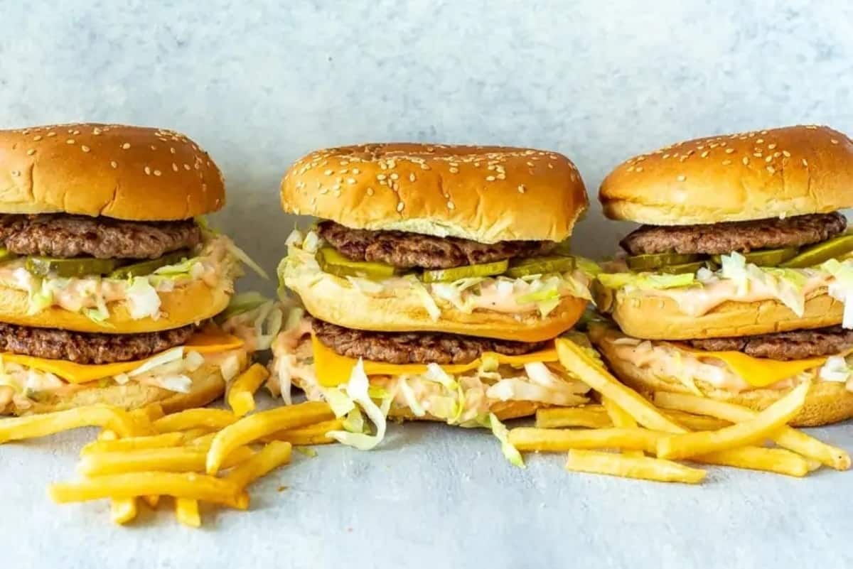 Three cheeseburgers with lettuce and condiments served with a side of french fries.