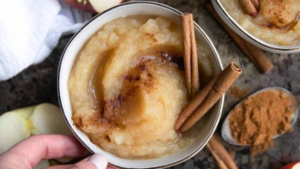 A bowl of applesauce garnished with a cinnamon stick and dusted with ground cinnamon.