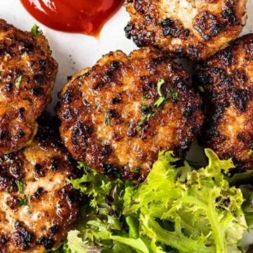 Grilled chicken burgers on a plate with salad and ketchup.