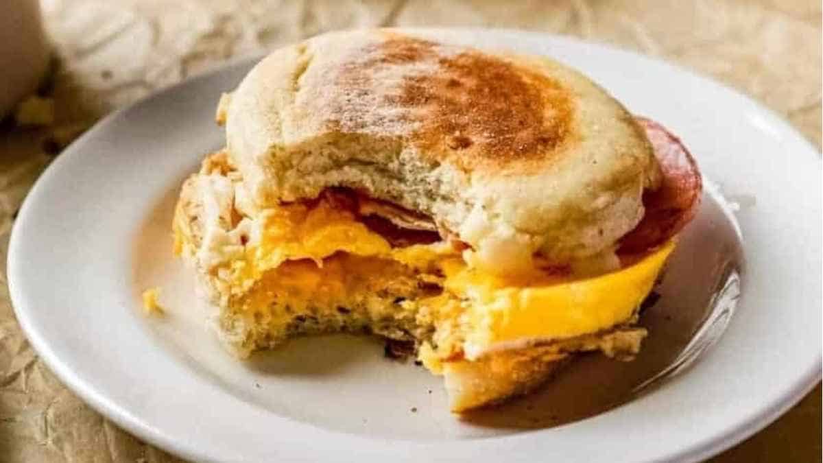 A breakfast sandwich on a plate with a cup of coffee.