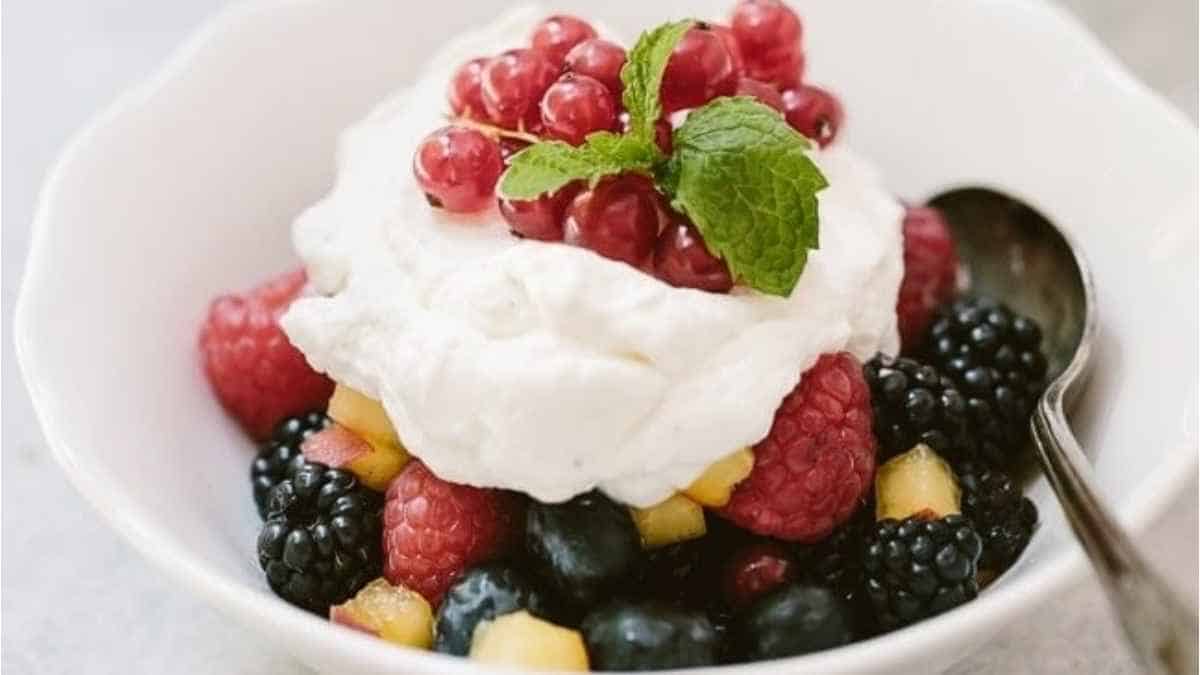A white bowl with berries and whipped cream.
