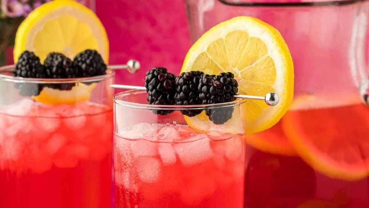 A pitcher of blackberry lemonade with lemon slices and blackberries.