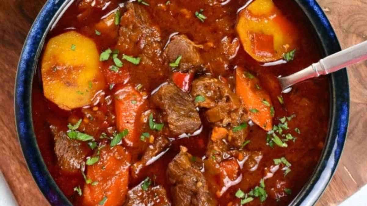 A bowl of hearty beef stew with carrots, potatoes, and garnished with herbs.