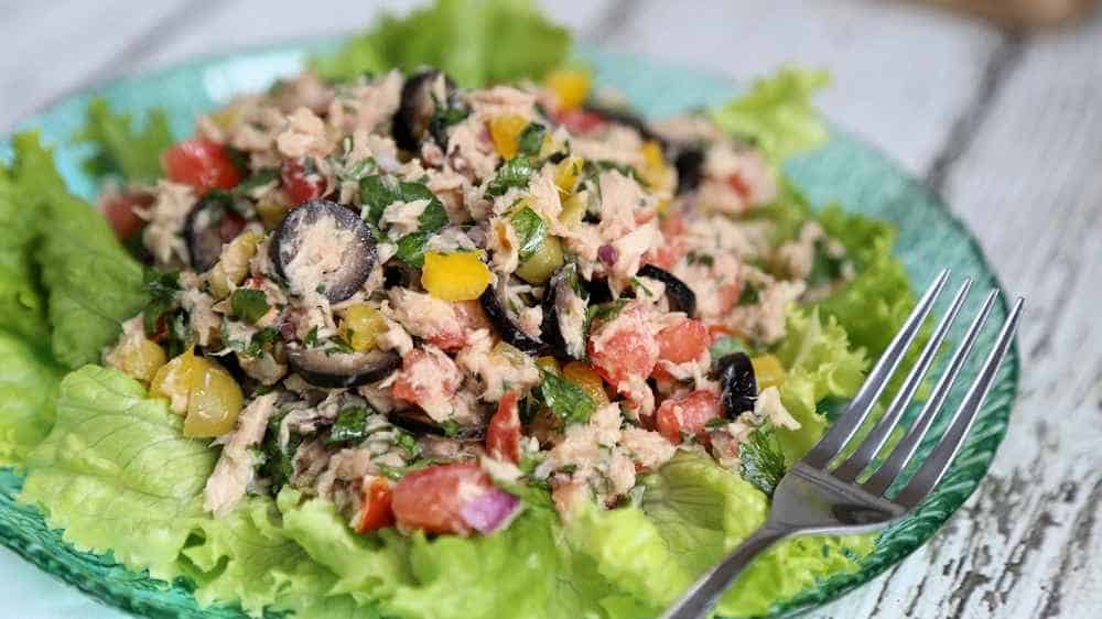 A fresh tuna salad with leafy greens, tomatoes, black olives, and bell peppers, served on a plate with a fork on the side.
