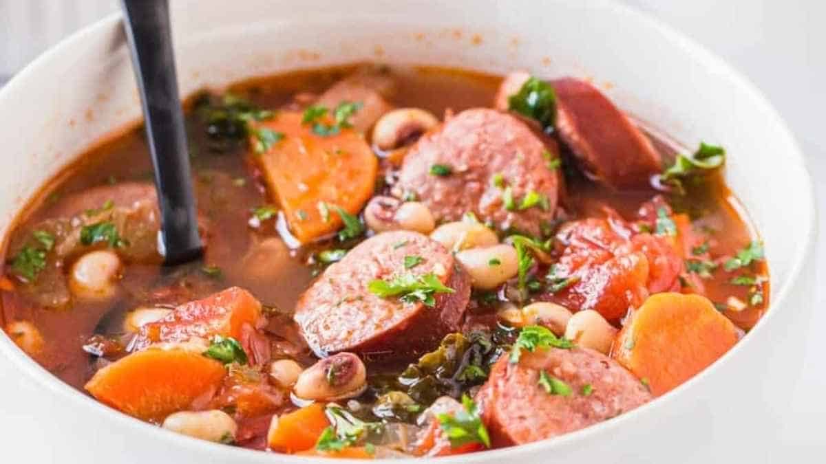 Hearty bean and sausage soup in a white bowl with a spoon.