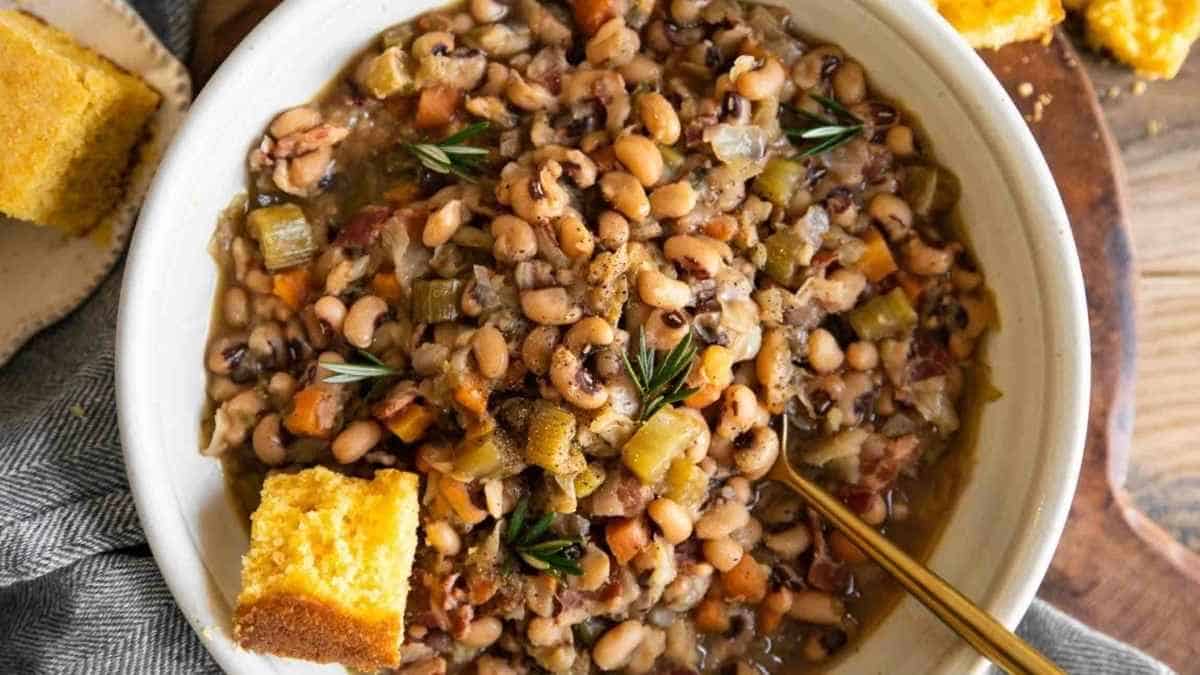 A bowl of mixed bean soup garnished with rosemary, served with cornbread on the side.