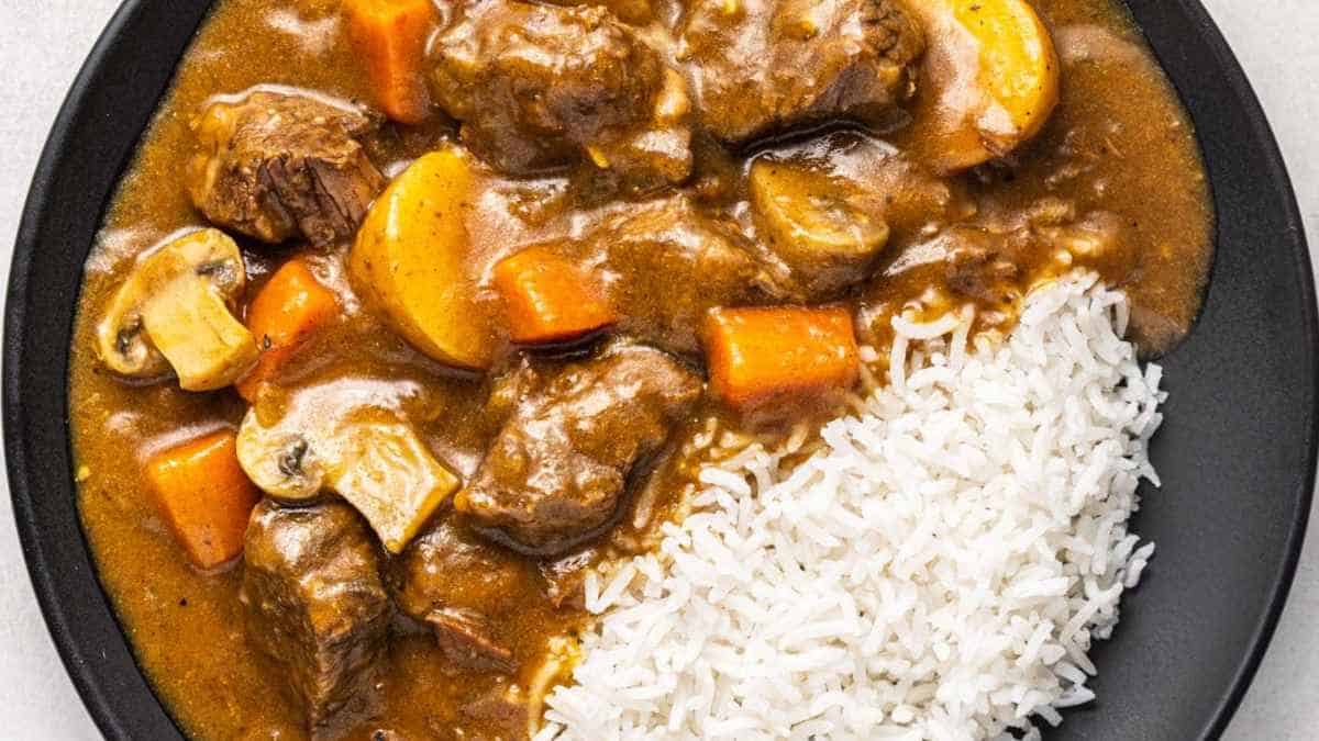 A plate of beef stew with carrots, mushrooms, and a side of white rice.