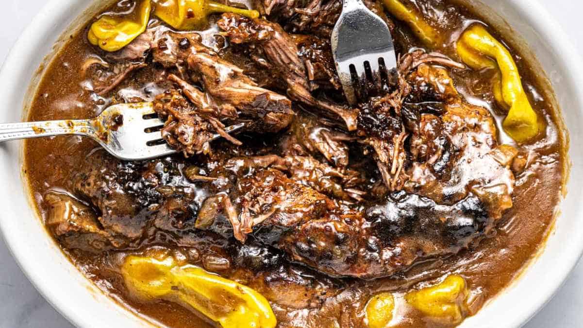 Beef stew with peppers and a fork in a white bowl.