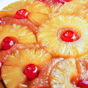 A pineapple upside-down cake garnished with cherries on a white plate.