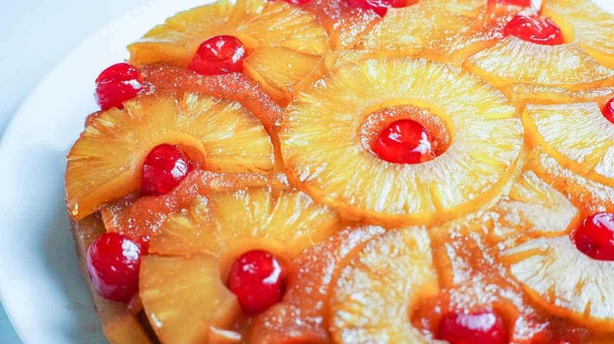 A pineapple upside-down cake garnished with cherries on a white plate.
