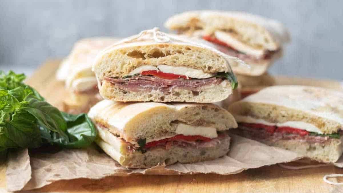 Halved italian sandwiches with salami and cheese on a wooden board.