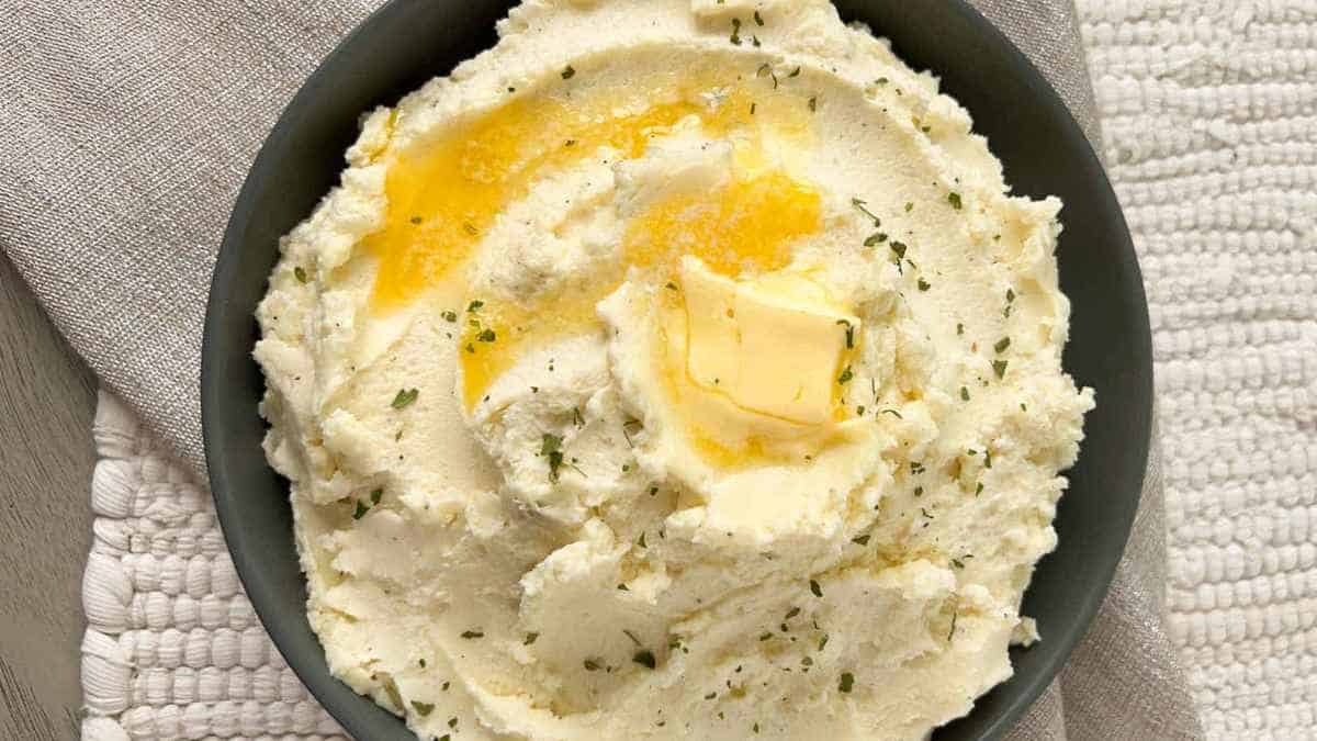 Bowl of creamy mashed potatoes topped with a pat of melted butter and a sprinkle of herbs.