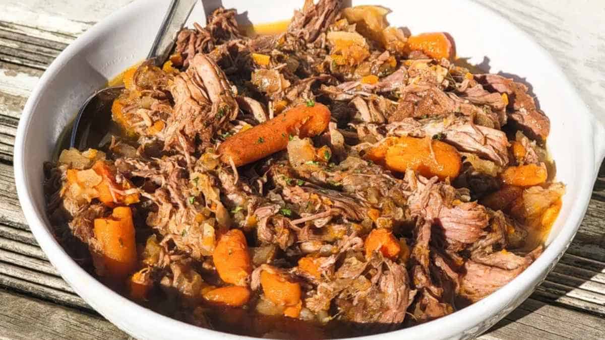 A bowl of pulled meat stew with carrots and potatoes.