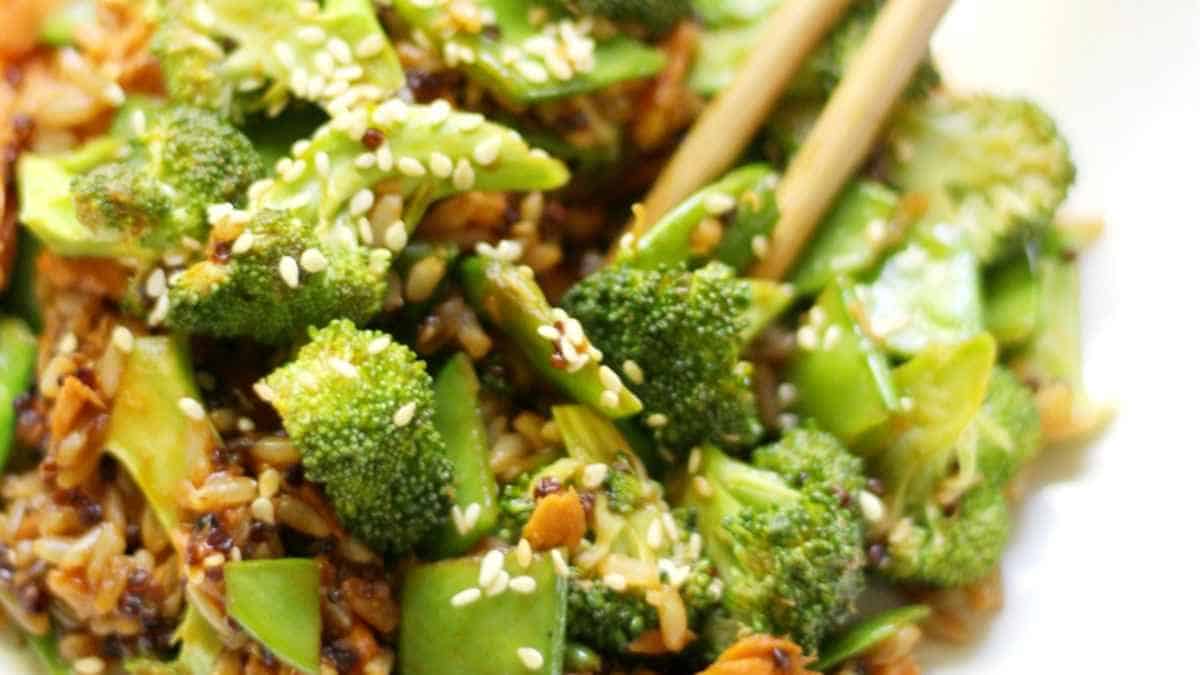Stir-fried broccoli with sesame seeds and chopsticks on top.