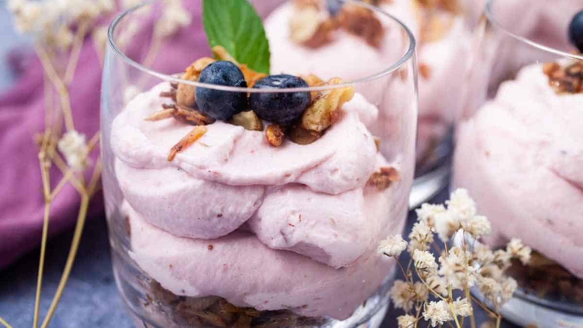 Blueberry mousse dessert garnished with fresh berries and nuts served in a glass.