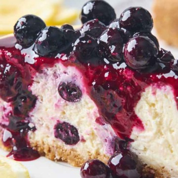 A slice of blueberry cheesecake with berry topping on a white plate.