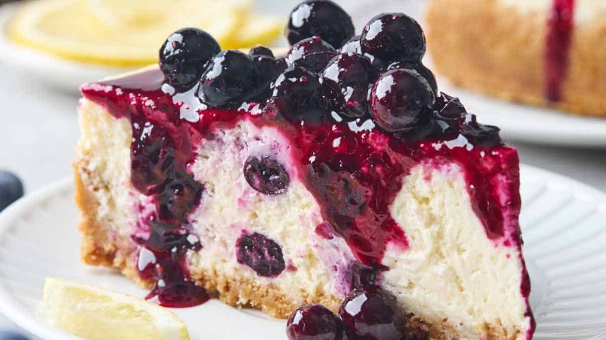 A slice of blueberry cheesecake with berry topping on a white plate.