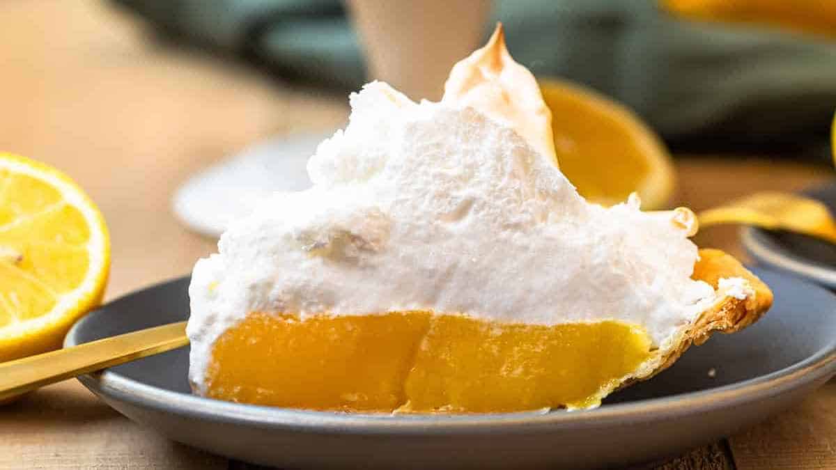 A slice of lemon meringue pie with fluffy white topping on a gray plate.