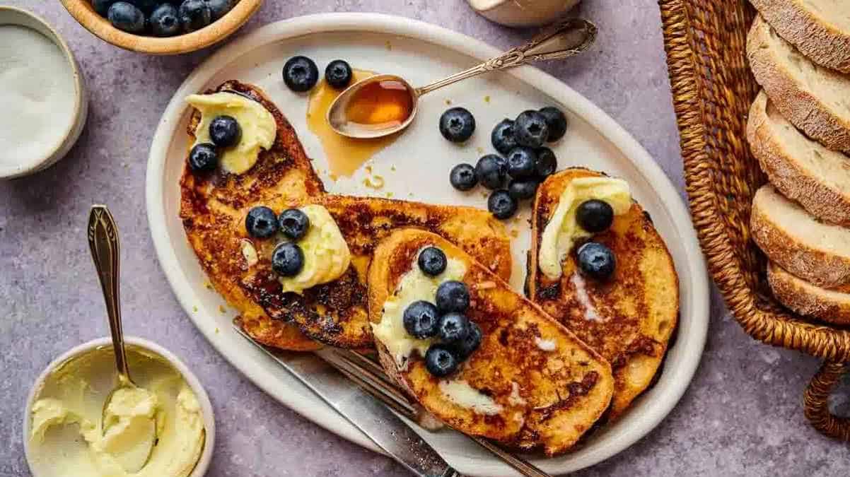 French toast served with blueberries and drizzled with syrup on a white plate.