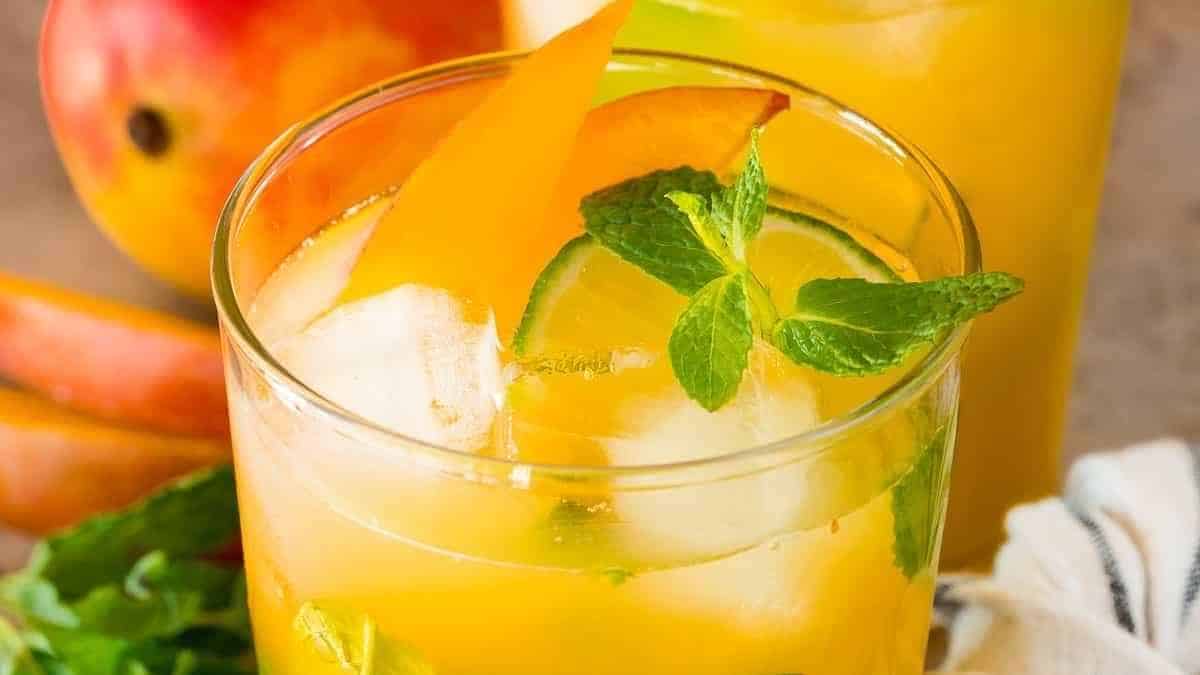A glass of peach mojito with mint leaves and a slice of peach.