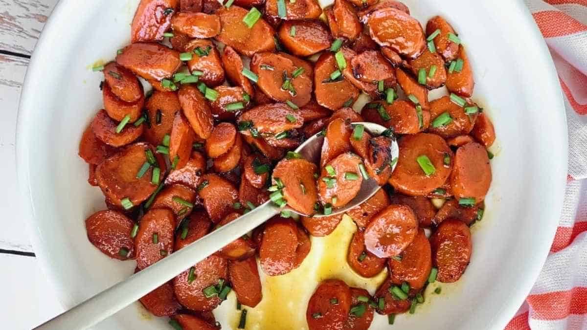 Roasted carrots in a white bowl with a spoon.