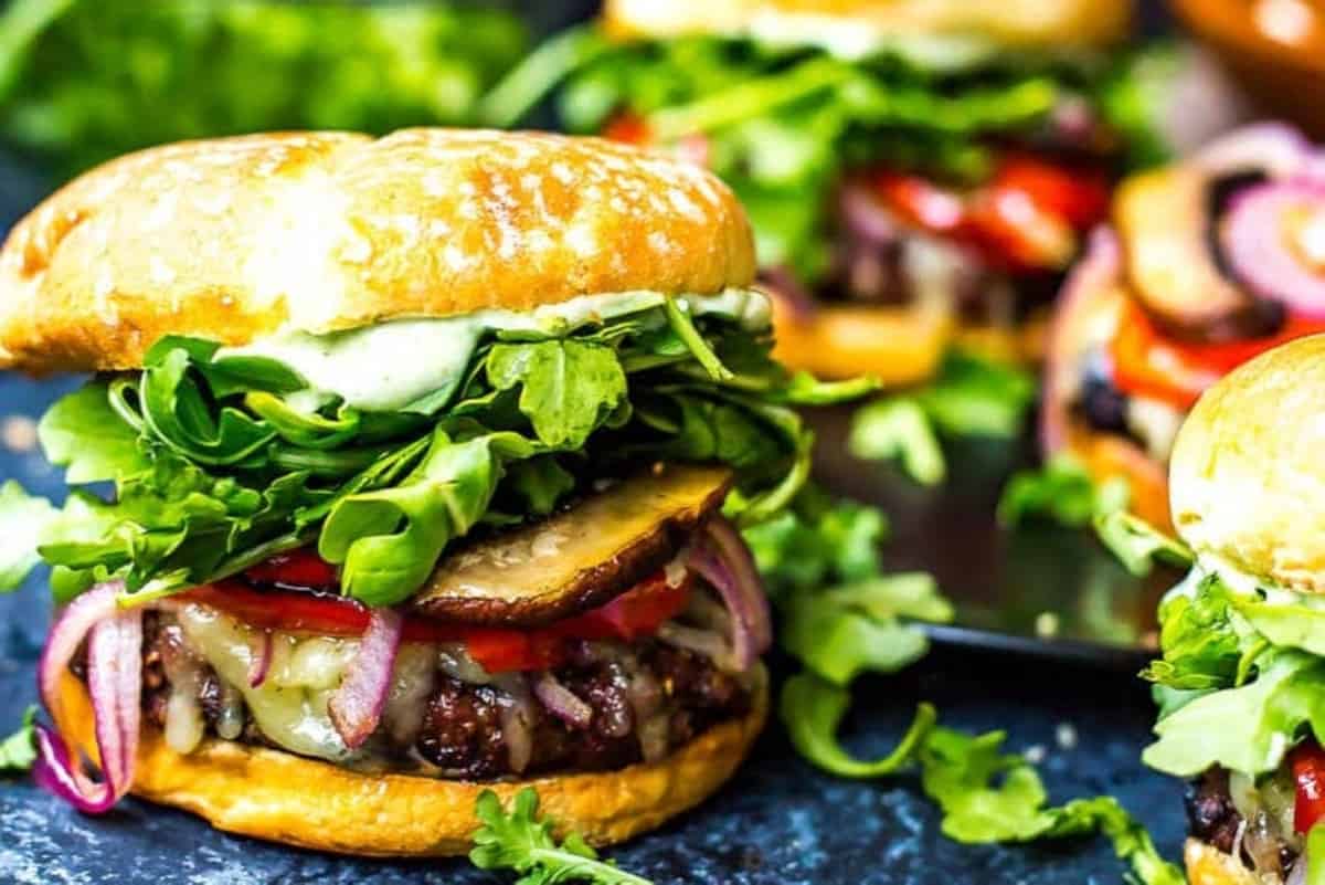 Gourmet burger with beef patty, grilled vegetables, and fresh greens on a sesame seed bun.