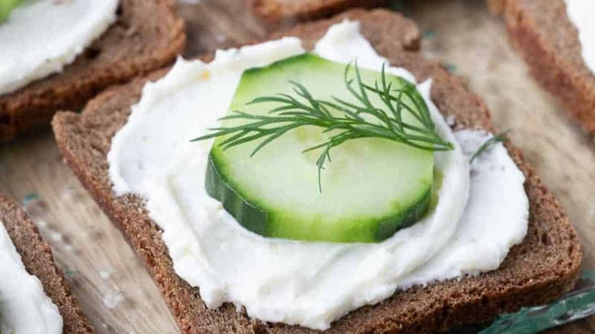 A slice of brown bread topped with cream cheese, cucumber, and dill.