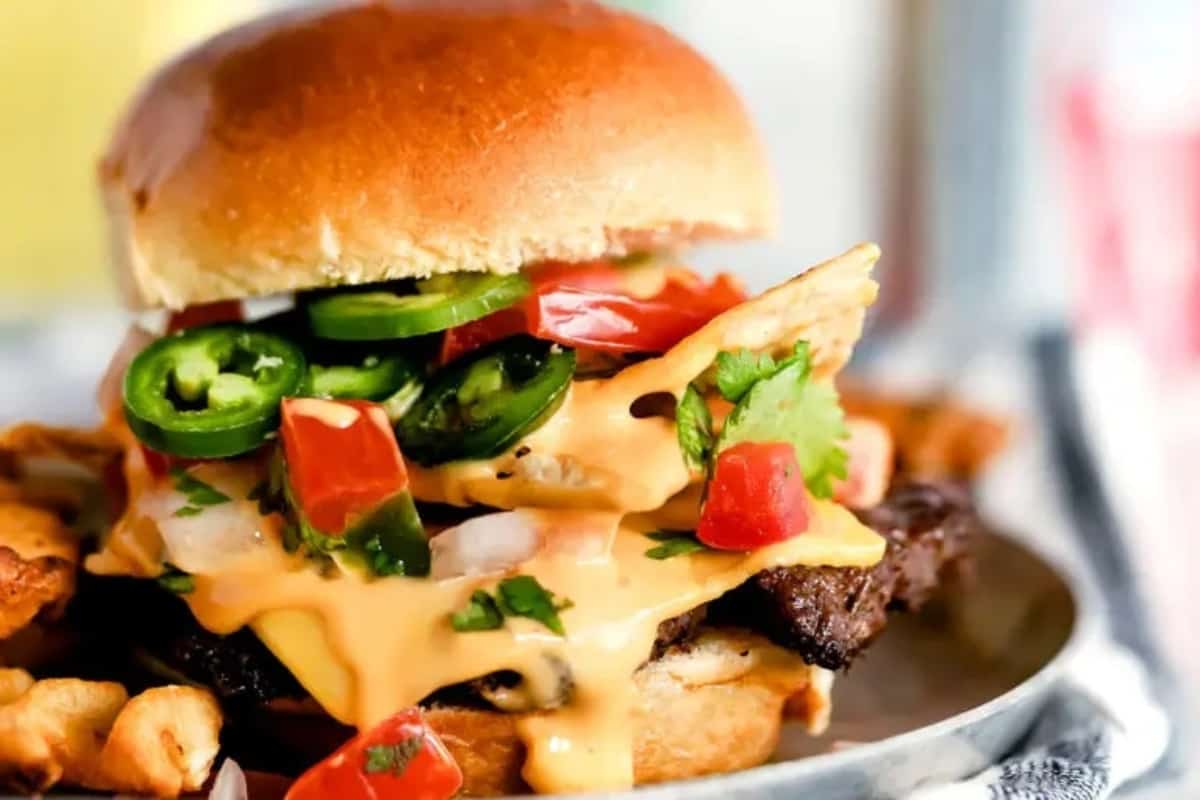 A loaded burger with cheese, jalapeños, tomatoes, and herbs on top of fries.