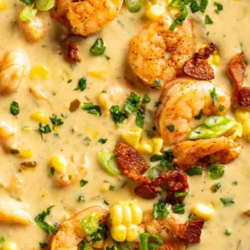 A bowl of creamy seafood chowder garnished with shrimp, corn, green onions, and bacon bits.