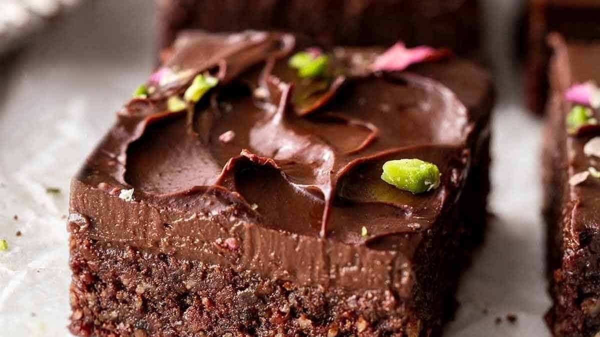 A slice of chocolate brownie with pistachios on top.