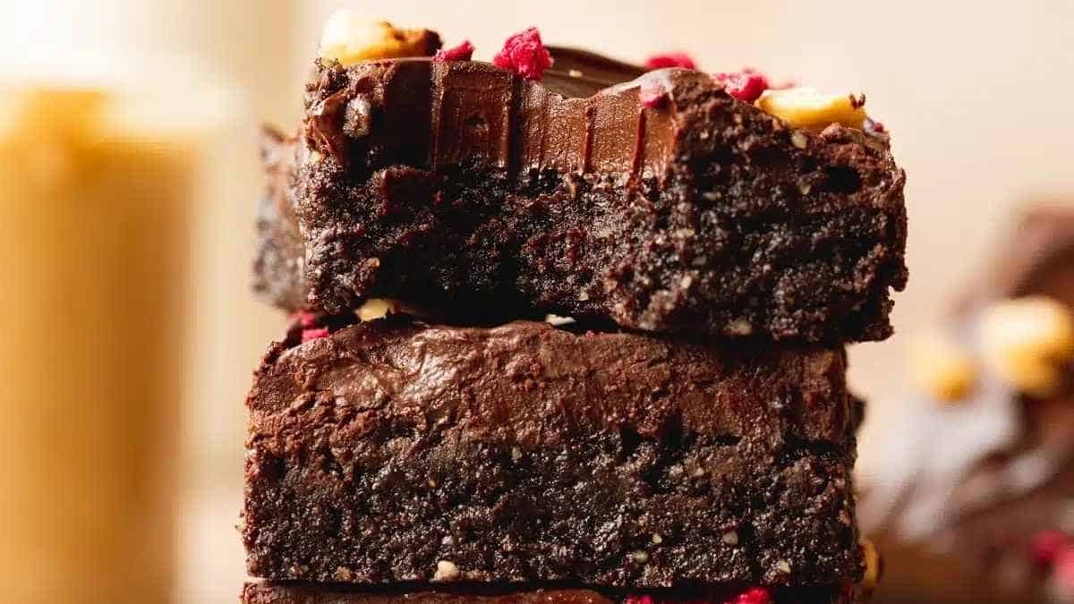 A stack of brownies with nuts and raspberries.