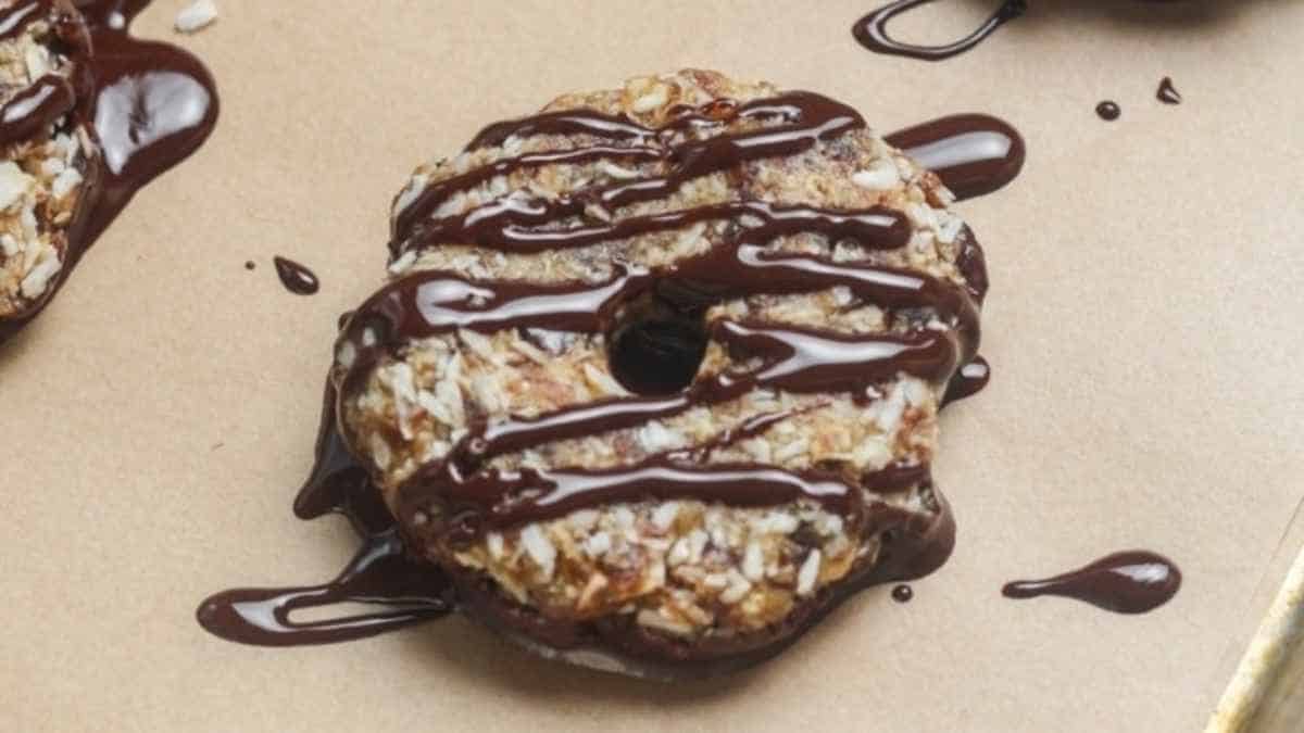 Donuts covered in chocolate drizzle on a baking sheet.