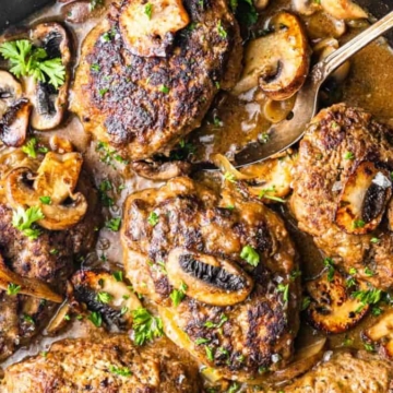 A skillet containing salisbury steaks with mushroom gravy, garnished with parsley.
