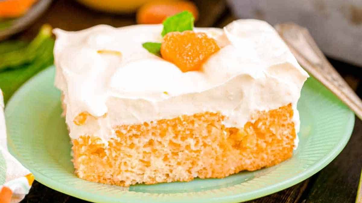 A slice of frosted cake topped with whipped cream and a piece of fruit, served on a teal plate.