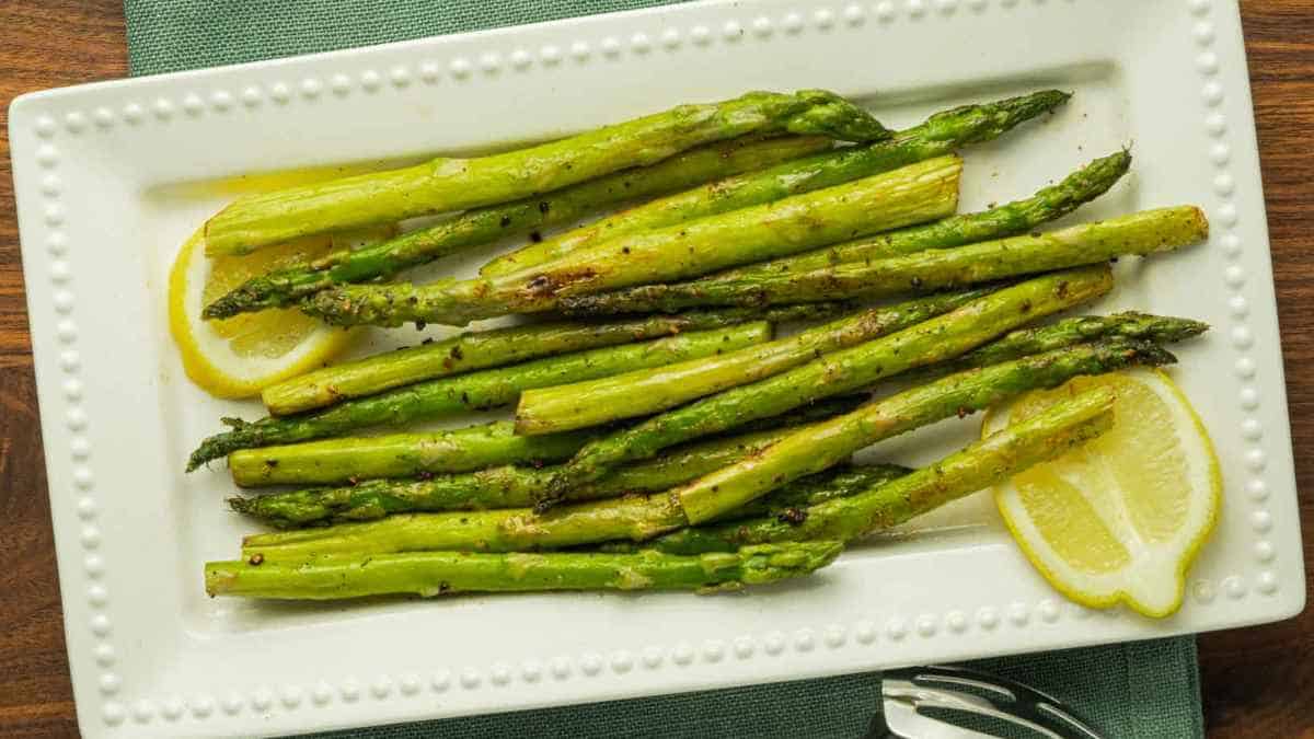 Grilled asparagus with lemon slices on a white serving plate.