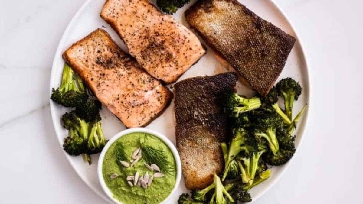 A plate with salmon, broccoli and pesto sauce.