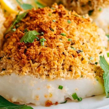 Baked white fish fillets topped with a golden breadcrumb crust, garnished with fresh parsley and lemon slices.